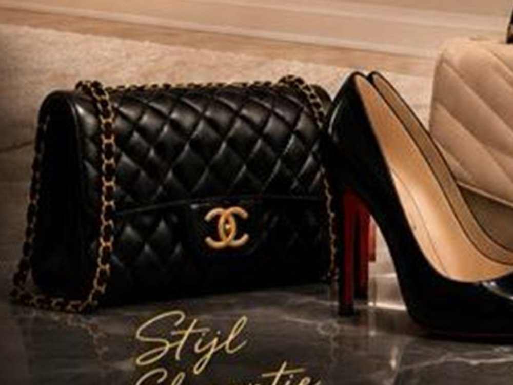 Zwarte gewatteerde designer handtas met gouden ketting naast hakken op marmer